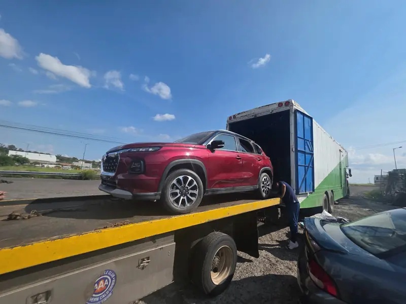 Red SUV loaded on a flatbed tow truck next to an Express Rico truck